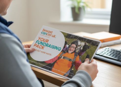 man in home office looking at printed out Breast Cancer UK fundraising pack
