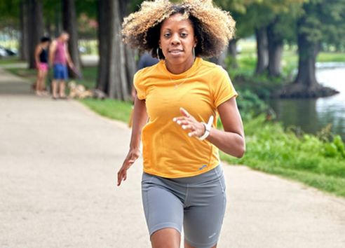 Middle aged woman in orange Tshirt running through park