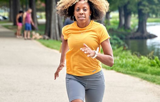 Middle aged woman in orange Tshirt running through park