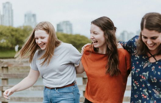 Three young adult women walking with linked arms and laughing